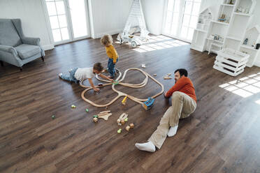 Vater liegt auf dem Boden neben seinem Sohn, der zu Hause mit einem Spielzeugeisenbahnset spielt - VPIF06266