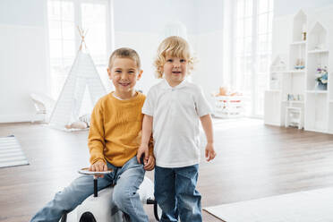 Happy boy with brother sitting on toy car at home - VPIF06274