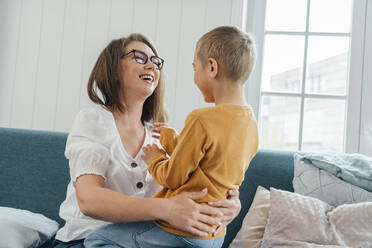 Cheerful mother with son sitting on sofa in living room at home - VPIF06280