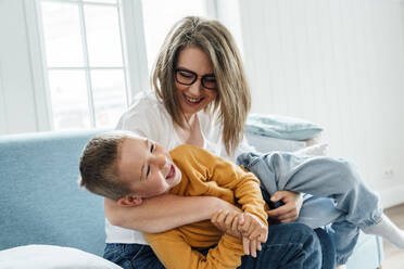 Glückliche Frau spielt mit Sohn auf Sofa im Wohnzimmer zu Hause - VPIF06282