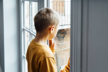 Boy looking through window at home - VPIF06291
