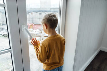 Junge schaut durch ein Glasfenster zu Hause - VPIF06292