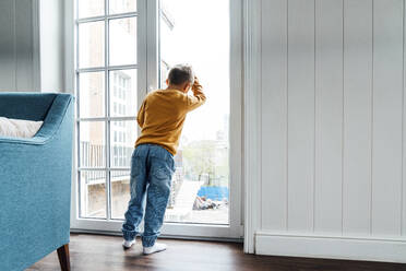 Boy leaning on glass window at home - VPIF06293