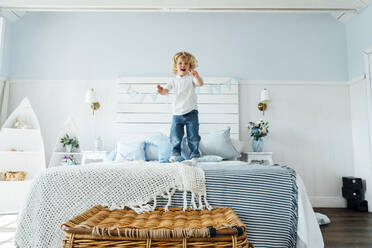 Cute boy jumping on bed at home - VPIF06299