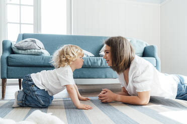 Mother and son staring at each other by sofa in living room at home - VPIF06304