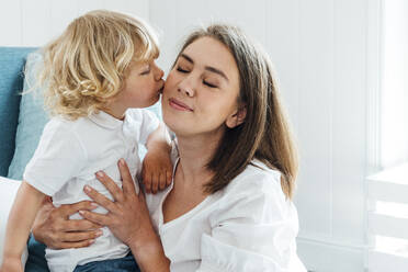 Cute boy kissing mother on cheek at home - VPIF06305