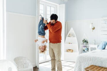 Father holding son upside down standing in bedroom at home - VPIF06308