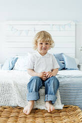 Cute boy sitting on bed at home - VPIF06311