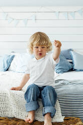 Boy gesturing with finger sitting on bed at home - VPIF06314