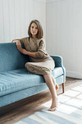 Smiling woman sitting on sofa in living room at home - VPIF06319