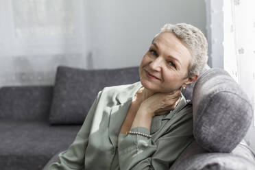 Porträt einer selbstbewussten reifen Frau, die auf der Couch im Wohnzimmer sitzt - LLUF00601