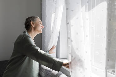 Mature woman at home looking out of window - LLUF00604