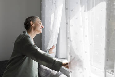 Reife Frau zu Hause mit Blick aus dem Fenster - LLUF00604