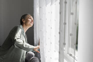 Mature woman at home looking out of window - LLUF00605