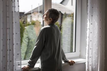 Reife Frau steht am Fenster zu Hause - LLUF00606