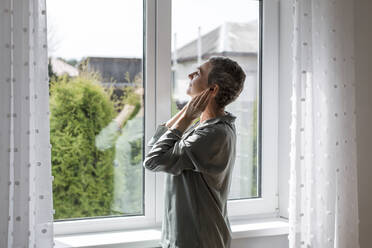 Reife Frau steht am Fenster zu Hause - LLUF00609