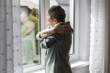 Reife Frau steht am Fenster zu Hause - LLUF00610