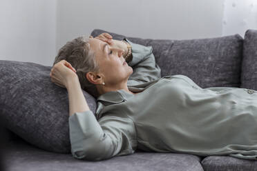 Mature woman lying on couch in living room with closed eyes - LLUF00628