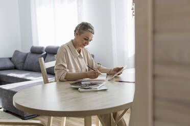 Frau benutzt digitales Tablet und macht sich Notizen am Tisch zu Hause - LLUF00641