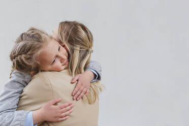 Tochter, die ihre Mutter umarmt, vor weißem Hintergrund - IHF00873