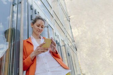 Smiling woman using smart phone leaning on glass door - OGF01271