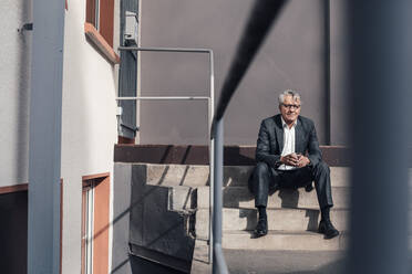 Senior businessman holding drinking glass on staircase - JOSEF10208