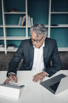 Älterer Geschäftsmann mit Tablet-PC und Laptop auf dem Schreibtisch im Büro - JOSEF10213