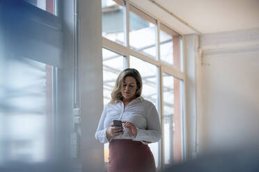 Businesswoman text messaging on smart phone at office - JOSEF10236