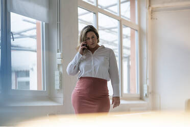 Selbstbewusste Geschäftsfrau mit Übergröße, die am Arbeitsplatz mit einem Smartphone telefoniert - JOSEF10254