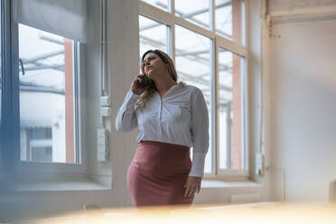 Geschäftsfrau mit Übergröße, die im Büro mit einem Mobiltelefon spricht - JOSEF10255