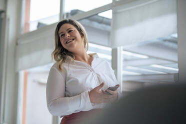 Happy businesswoman with smart phone at work place - JOSEF10264