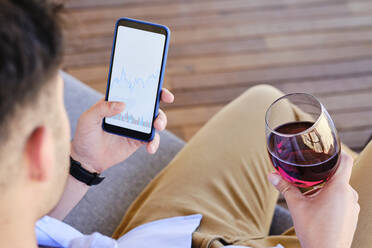 Mann hält Weinglas und Smartphone mit Börsendaten - AODF00615