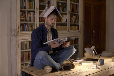 Man with book on head reading at home office - VEGF05655