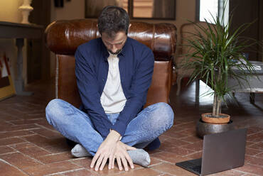 Man sitting cross-legged by laptop on floor at home - VEGF05664
