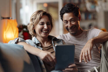 Happy couple using tablet PC sitting on sofa at home - JOSEF10288