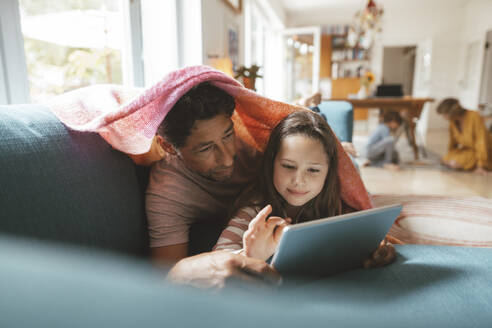 Mädchen mit Tablet-PC, das mit seinem Vater zu Hause auf dem Sofa liegt - JOSEF10291
