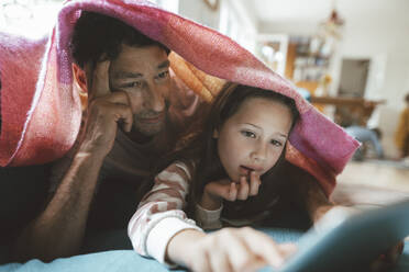 Father lying with daughter using tablet PC under blanket at home - JOSEF10292