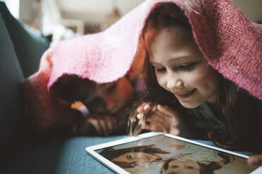 Junge liegt mit seiner Schwester und betrachtet ein Foto auf einem Tablet-PC zu Hause - JOSEF10297