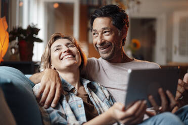 Glücklicher Mann und Frau mit Tablet-PC zu Hause sitzend - JOSEF10324
