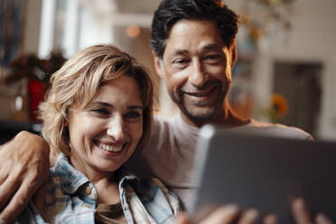 Happy woman sharing tablet PC with man at home - JOSEF10325