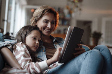 Happy woman sitting with daughter using tablet PC at home - JOSEF10337