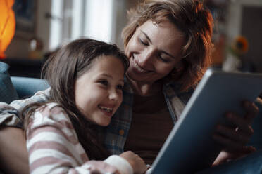 Glückliche Mutter und Tochter sitzen mit Tablet-PC zu Hause - JOSEF10338