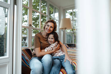 Happy mother and daughter sitting on sofa - JOSEF10347