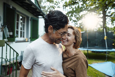 Happy woman embracing man wearing eyeglasses in back yard - JOSEF10353