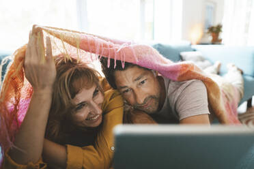 Glückliches Paar mit Tablet-PC unter einer Decke liegend zu Hause - JOSEF10362