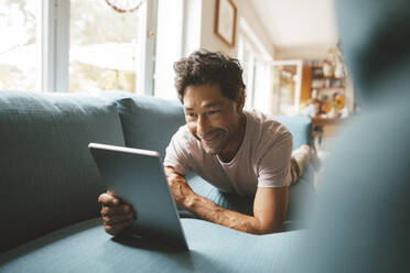 Glücklicher Mann mit Tablet-PC auf dem Sofa zu Hause - JOSEF10375