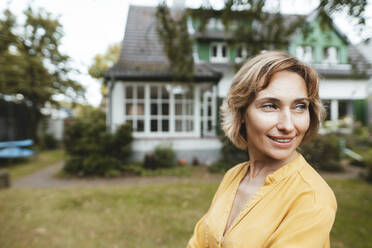 Happy woman standing in front of house - JOSEF10385