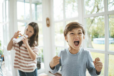 Boy screaming standing in front of sister playing musical instrument - JOSEF10392