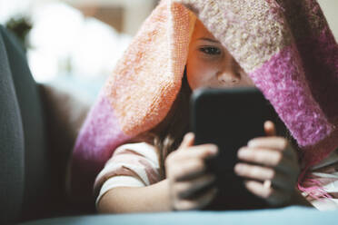 Mädchen, das ein Smartphone benutzt und zu Hause unter einer Decke liegt - JOSEF10399