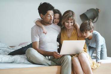 Family sharing laptop sitting on bed at home - JOSEF10403